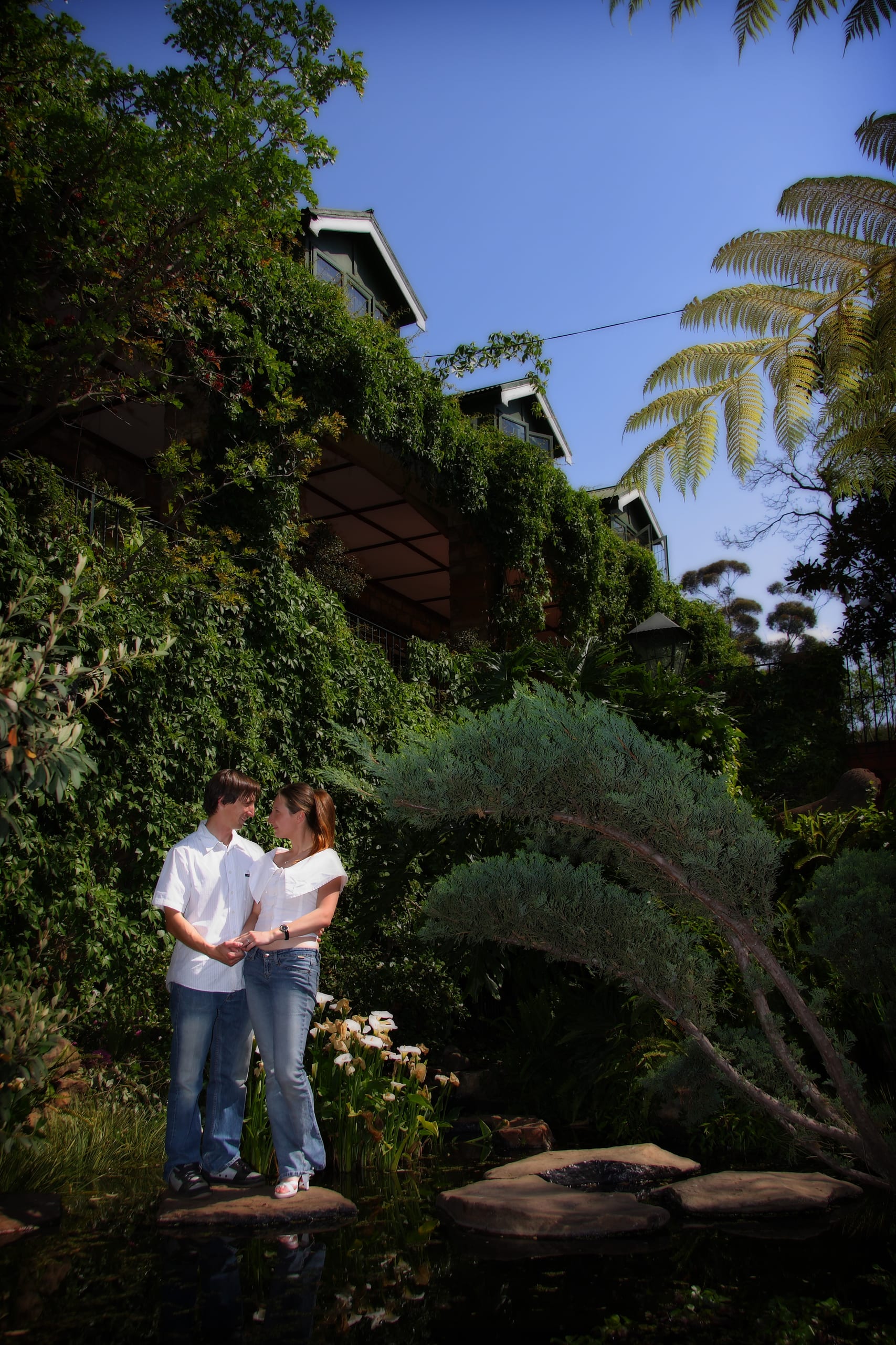Greg and Katje standing together beside a pond in a lush garden