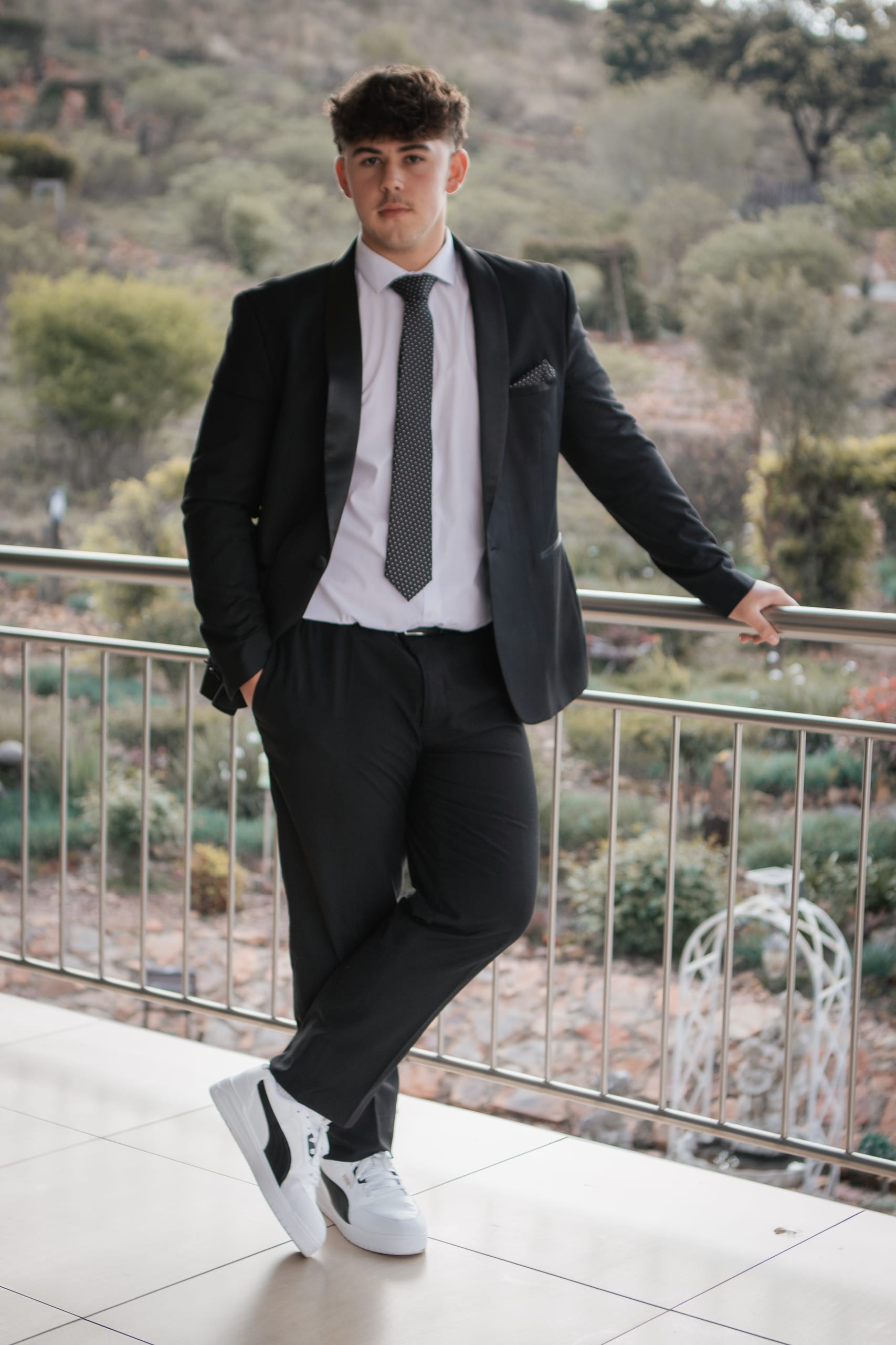 Matriculant posing alone in a black suit on a terrace